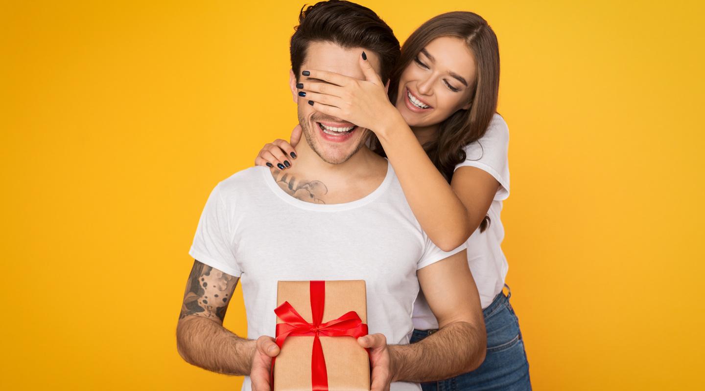 Article Cards Featured Image Girl covering her boyfriend eyes and giving him present on yellow background